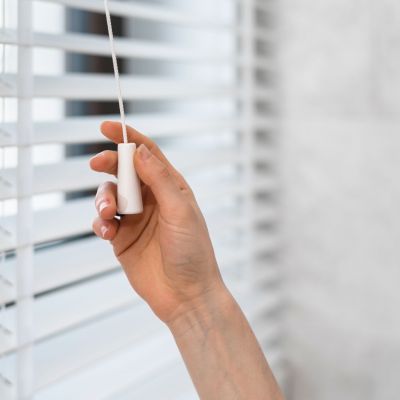 Cropped shot of woman hand pulls the adjustment string closing horizontal window blinds in tradition venetian style made from natural material. Concept of privacy and sunlight protection
